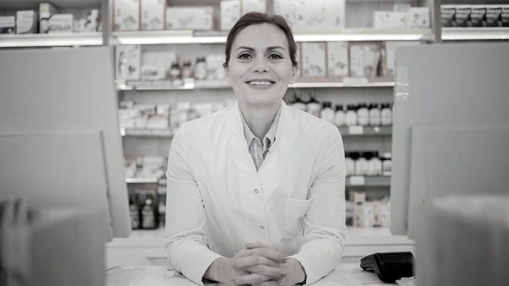 A female pharmacist smiling between two computers